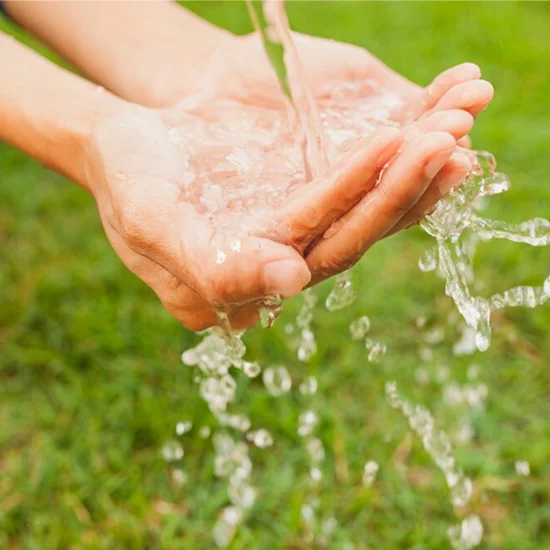 Hands cupped to catch clear water outdoors on grass surface in the background.
