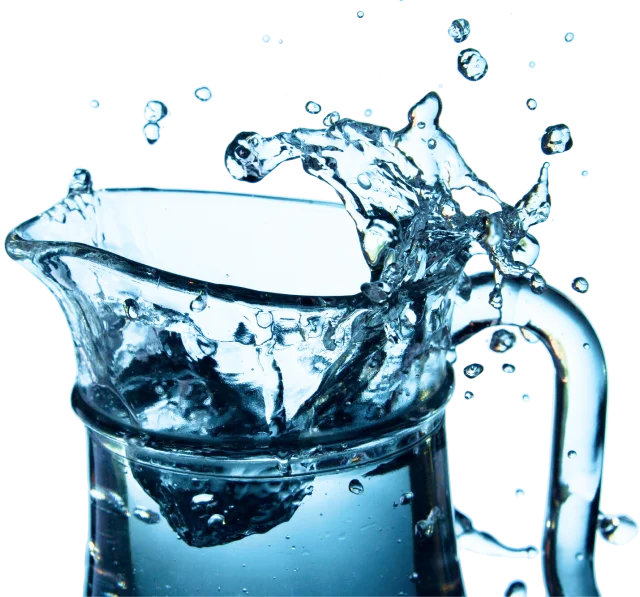 Glass pitcher filled with water, water splashing over the rim with droplets flying in the air.